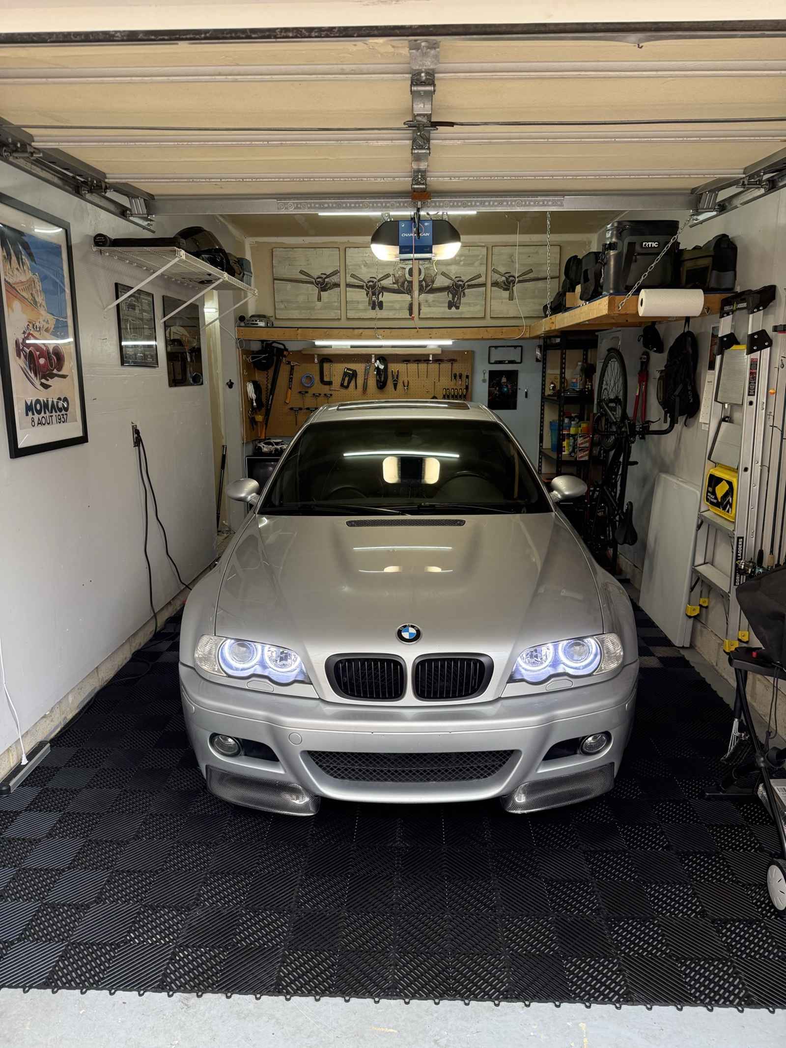 Silver car parked in an organized garage with tools, a bicycle and a ladder stored along the walls.